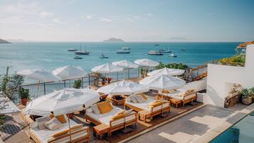 A deck with sun loungers and umbrellas overlooking a marina with boats.