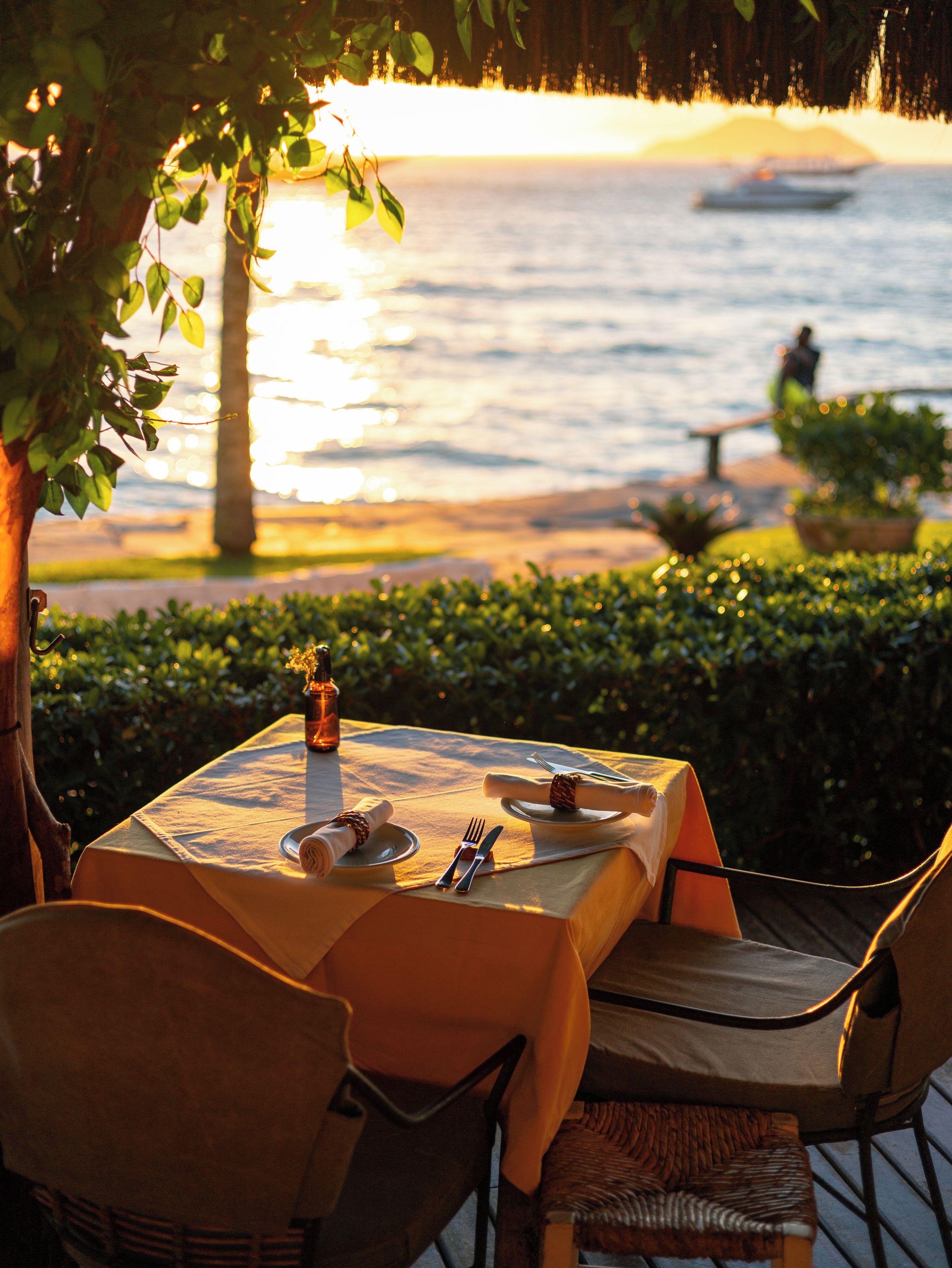 An outdoor dining table with a view of the sea and a person walking in the background.