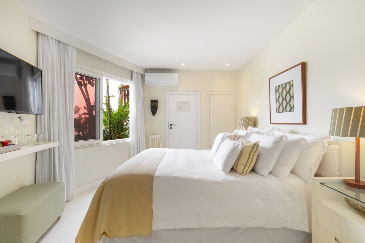 A hotel room with a bed, a TV, a window with curtains, and a door.