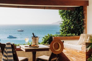 A terrace with a view of the sea, a table with a bottle of champagne, and a straw hat.