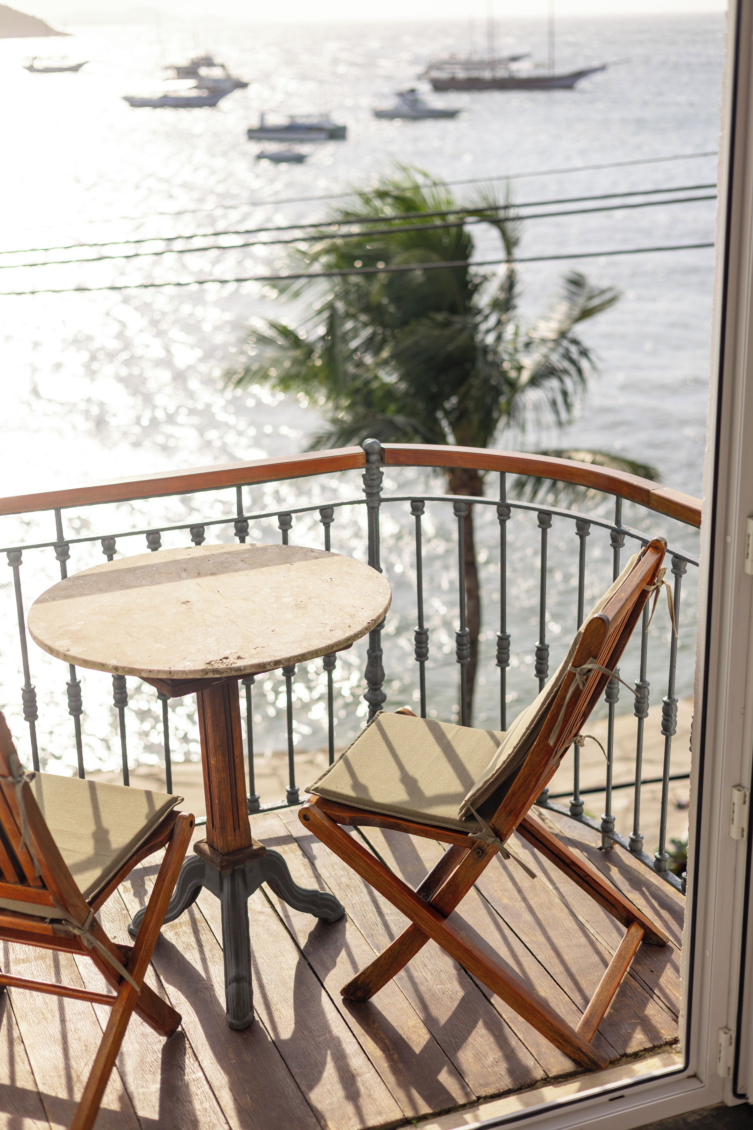 A wooden deck with a round table and two chairs, overlooking a body of water with boats.
