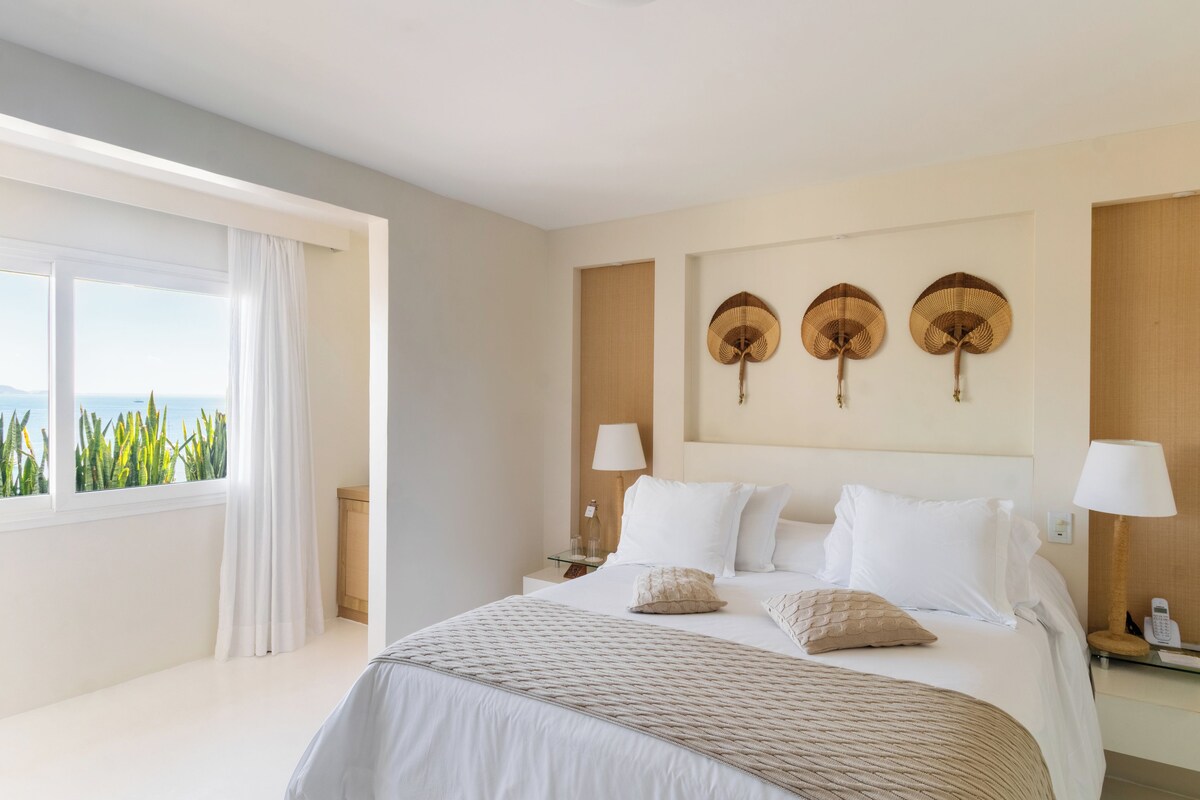 Habitación de hotel con una cama grande, dos mesitas de noche, una ventana con cortinas y vistas a zonas verdes.
