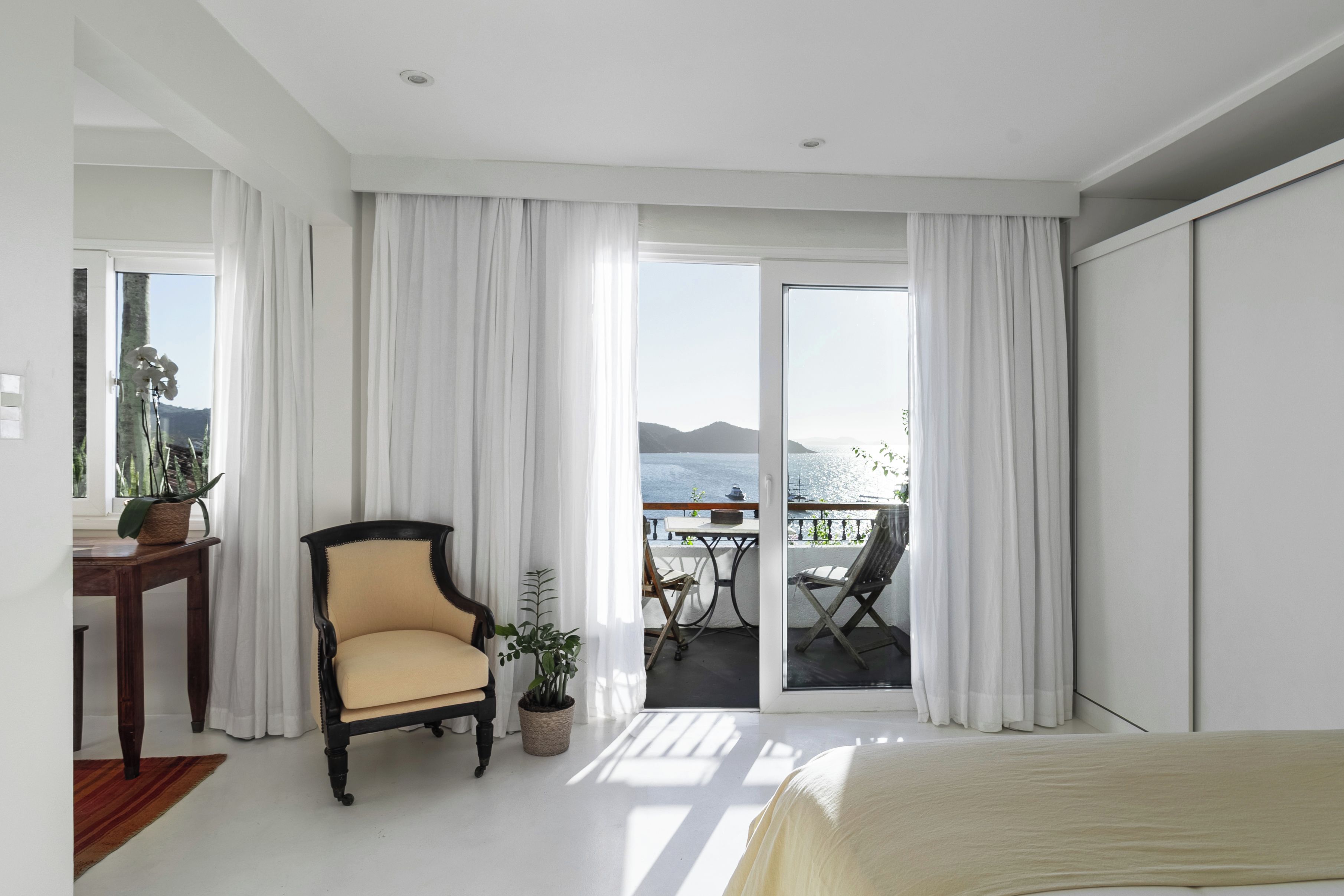 A hotel room with a bed, a chair, a table, and a view of the sea.