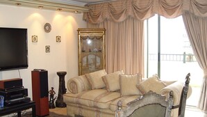 A living room with a large flat-screen TV, a wooden entertainment unit, a beige sofa, and a decorative mirror.