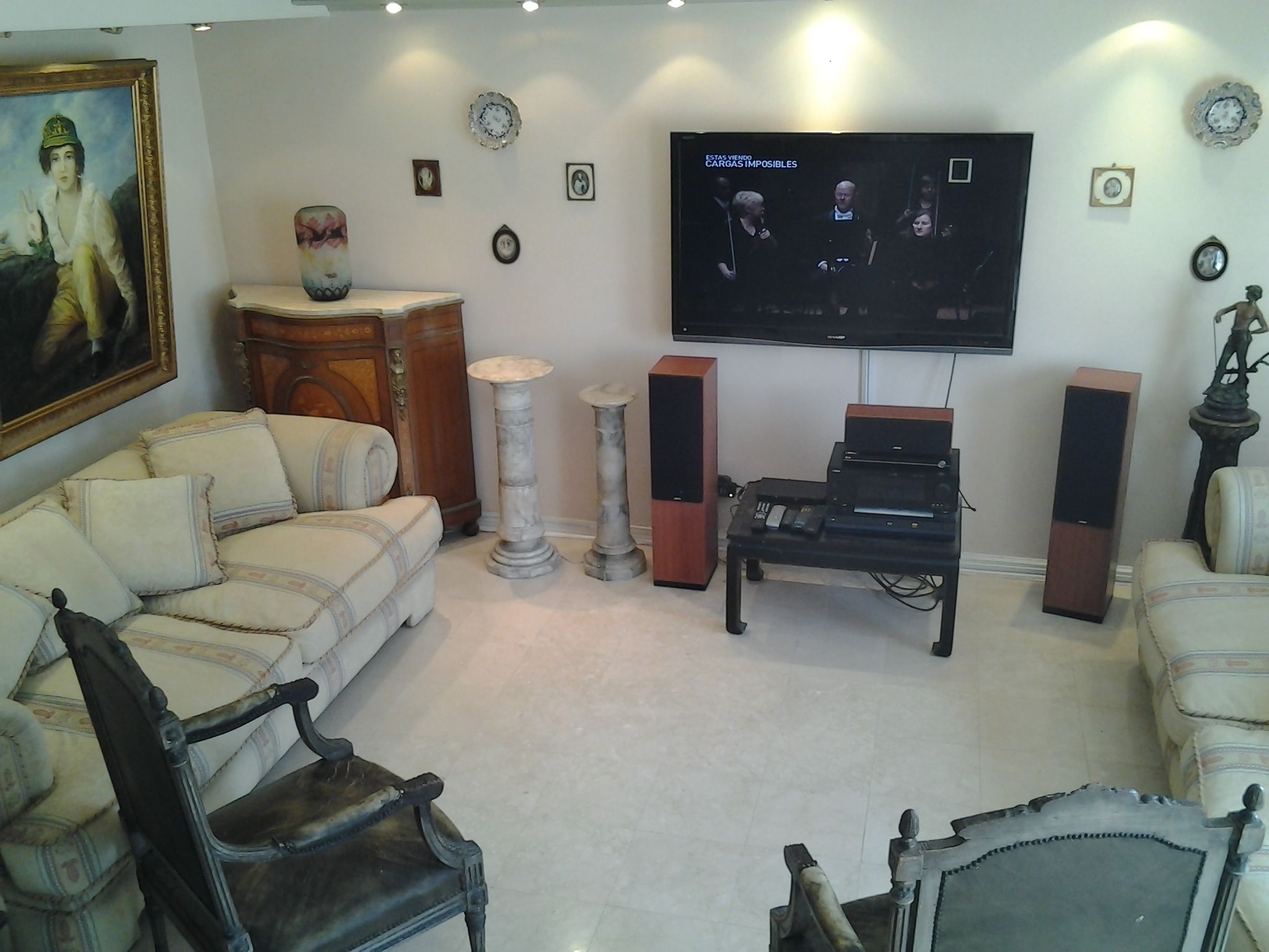 Una sala de estar con un sofá, un piano, altavoces y un televisor montado en la pared.