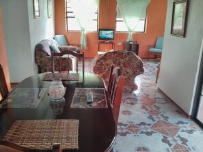 Un comedor con mesa de vidrio, sillas, televisor y sofá floral.
