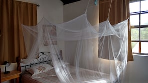 Una cama con dosel, una mesita de noche con lámpara y una ventana con cortinas.