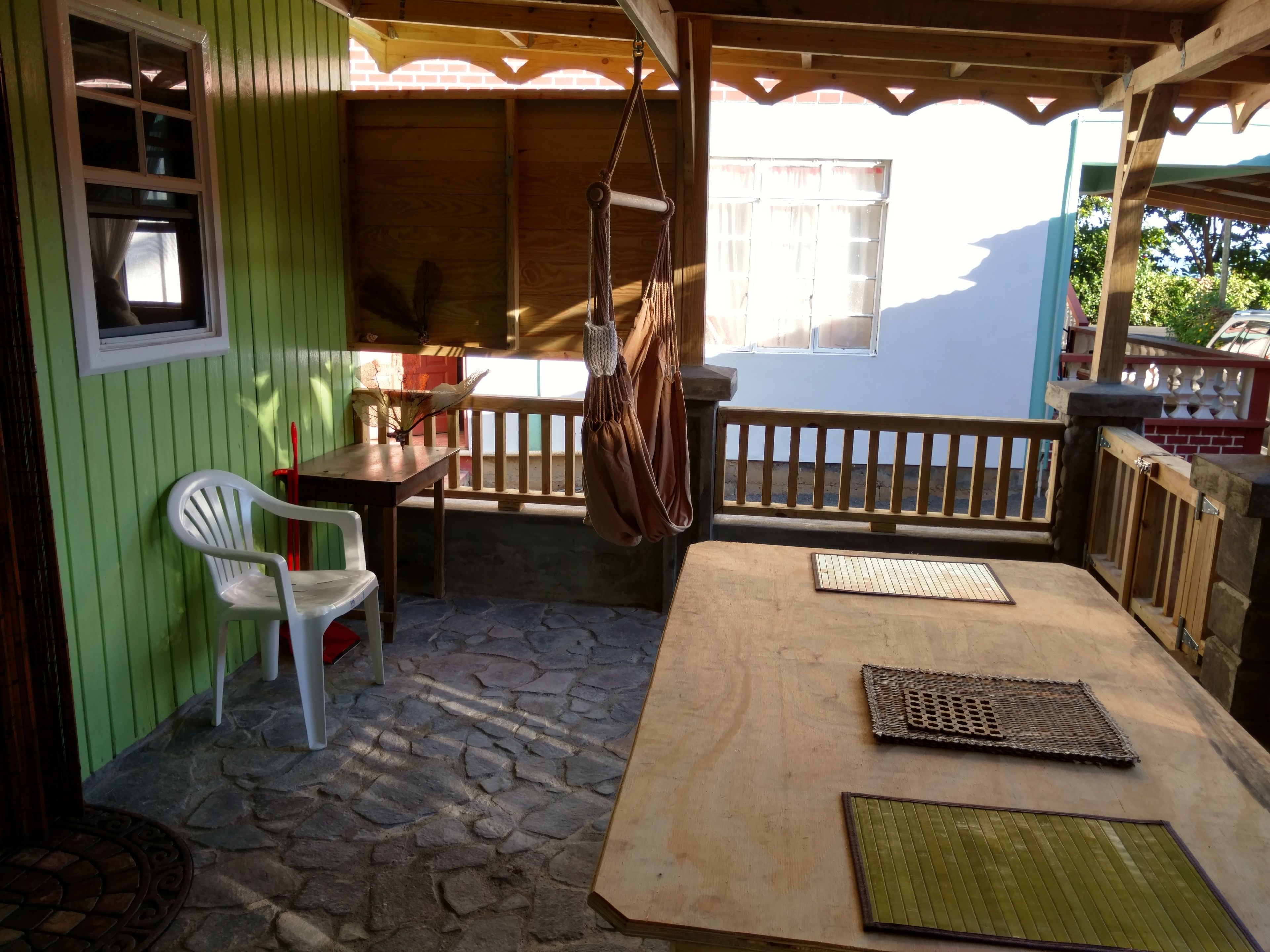 Un patio techado con mesa de madera, dos sillas y un bolso colgante.