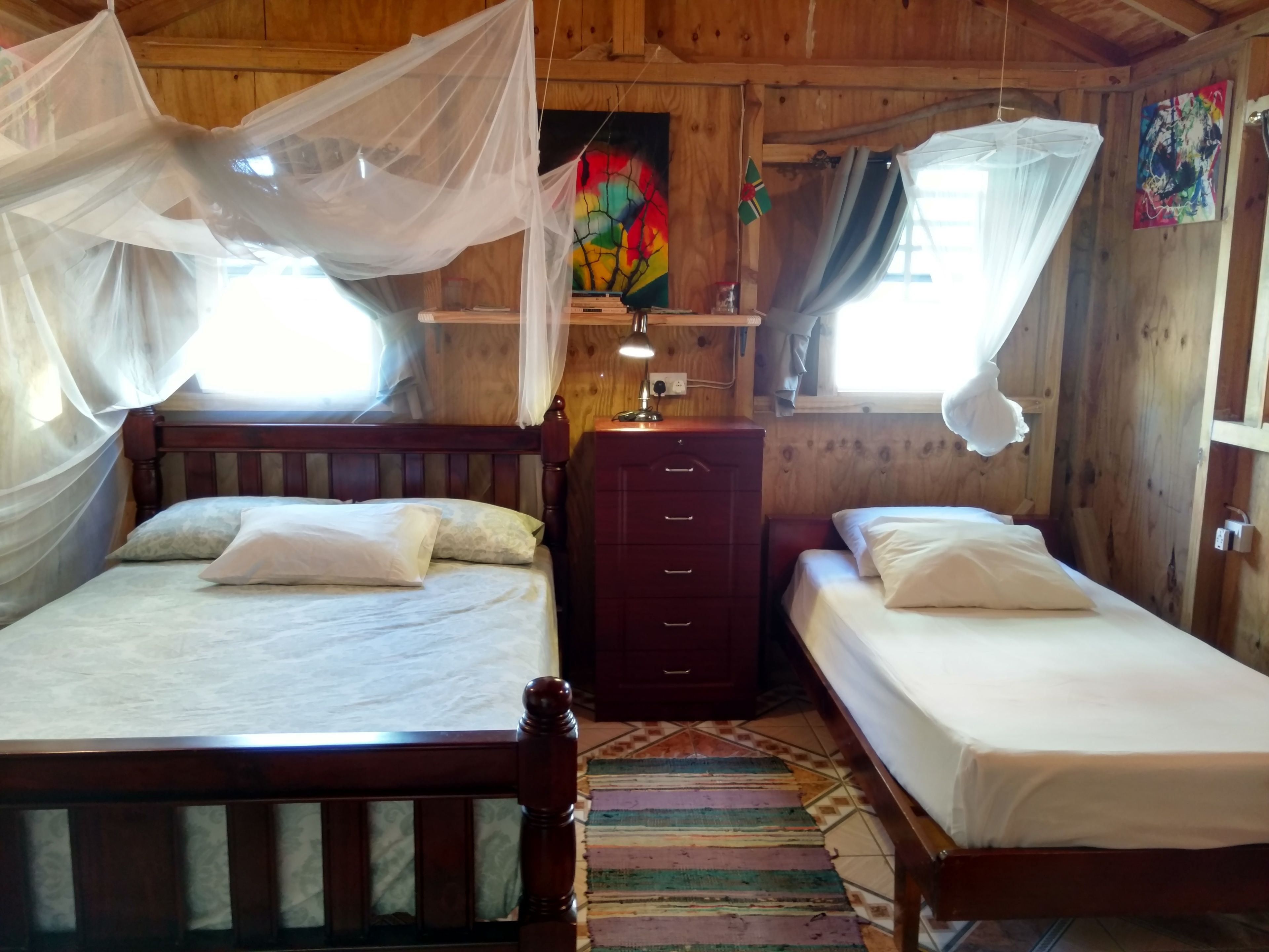 Una habitación de madera con dos camas, cada una con dosel. Hay un aparador de madera y un cuadro de colores en la pared.