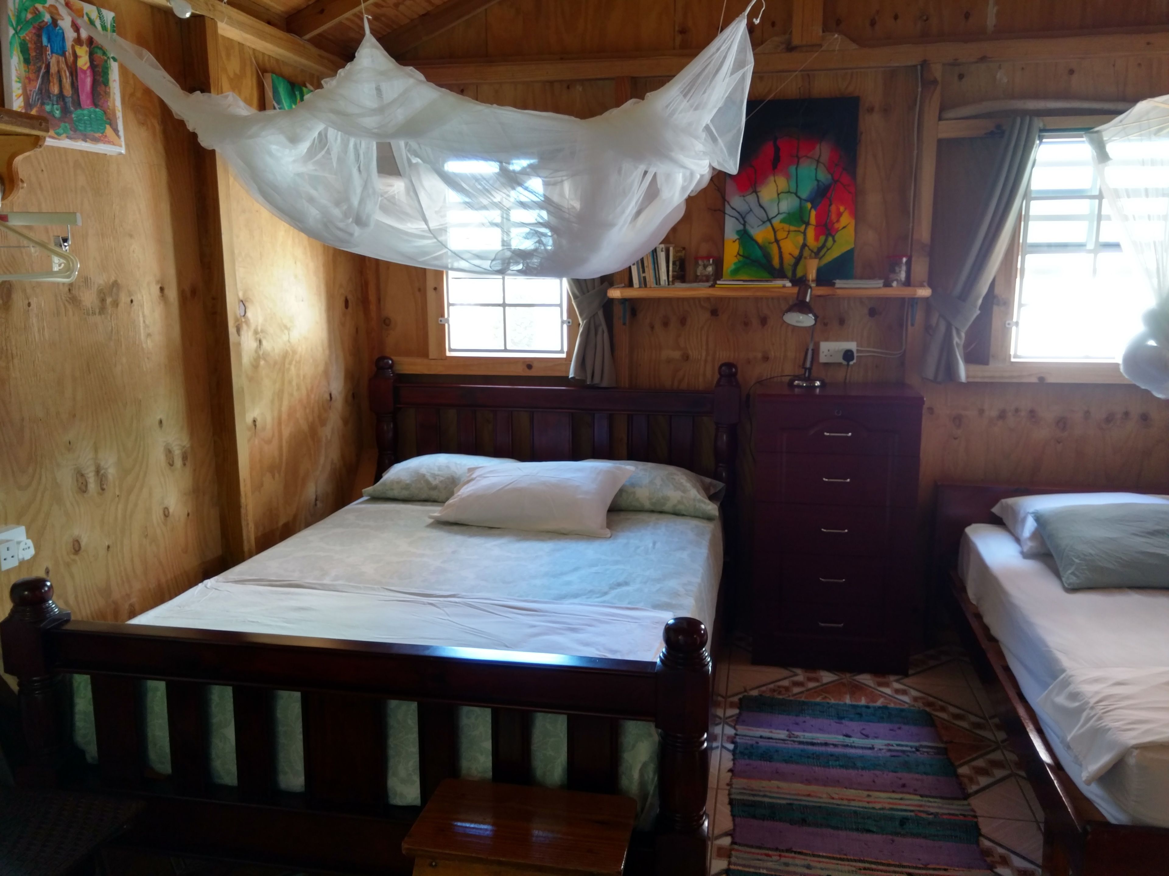 Um quarto de madeira com uma cama, mesa de cabeceira e janela.
