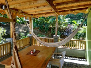 Una terraza de madera con una hamaca, una mesa con un tapete y sillas.