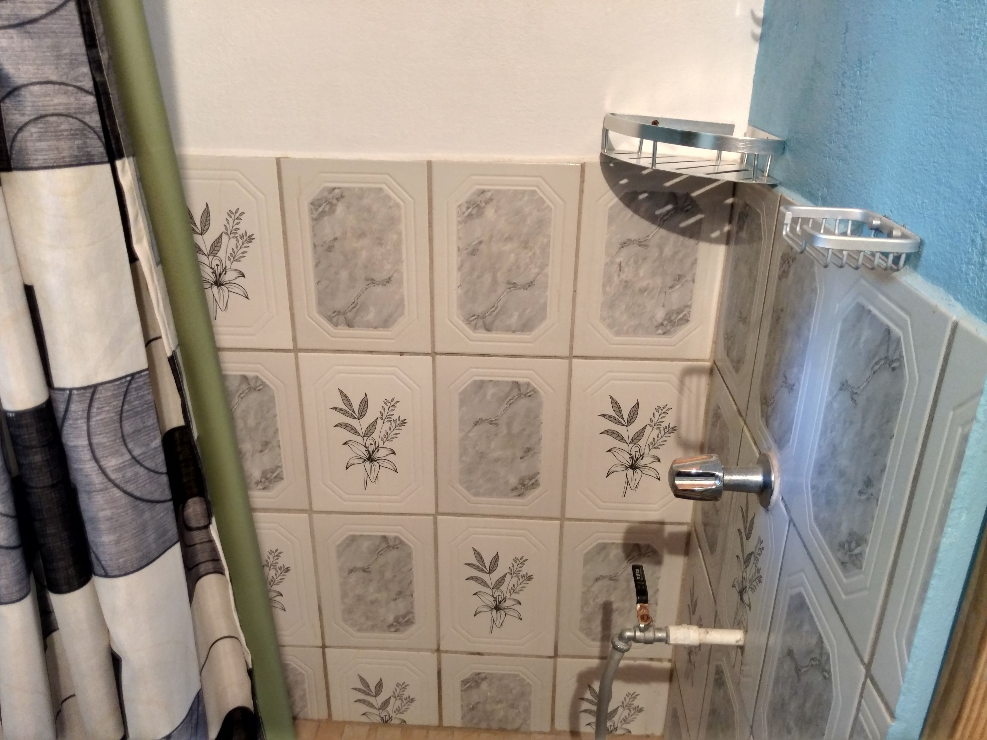 A bathroom with hexagonal tiles featuring floral patterns, a shower area with a chrome showerhead, and a towel rack.
