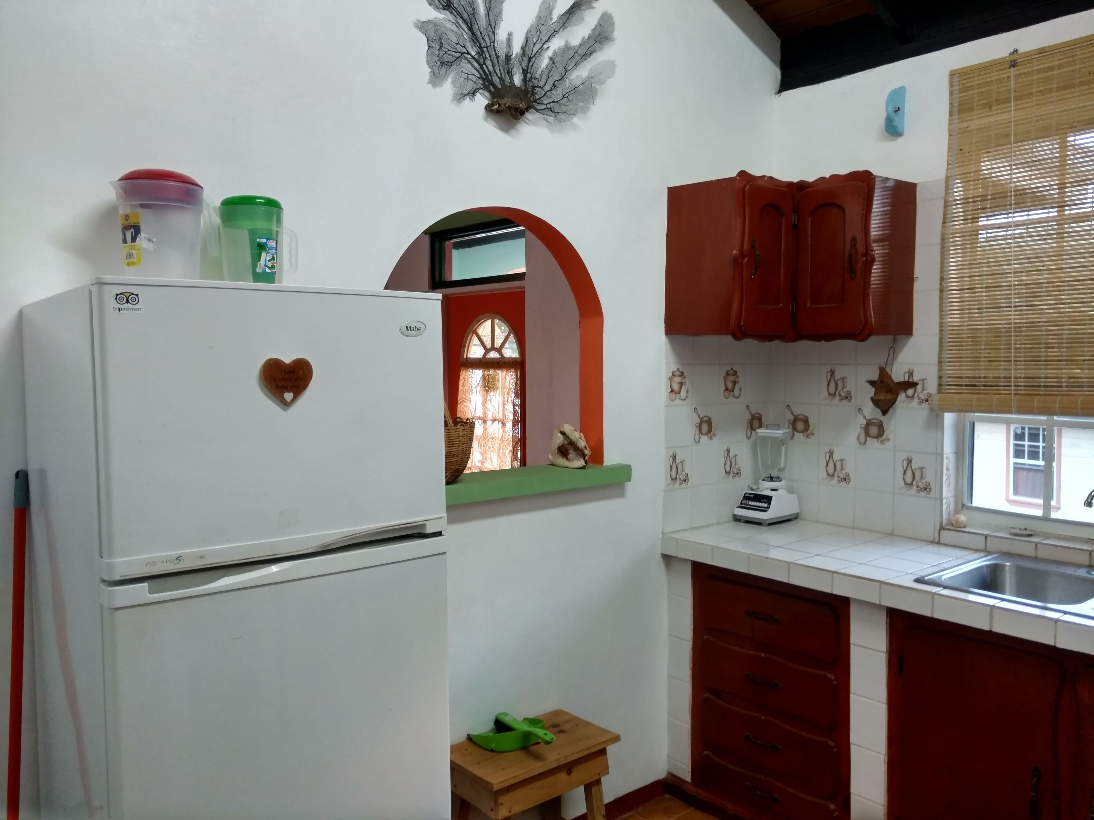 A compact kitchen with a refrigerator, a blender, and wooden cabinets.