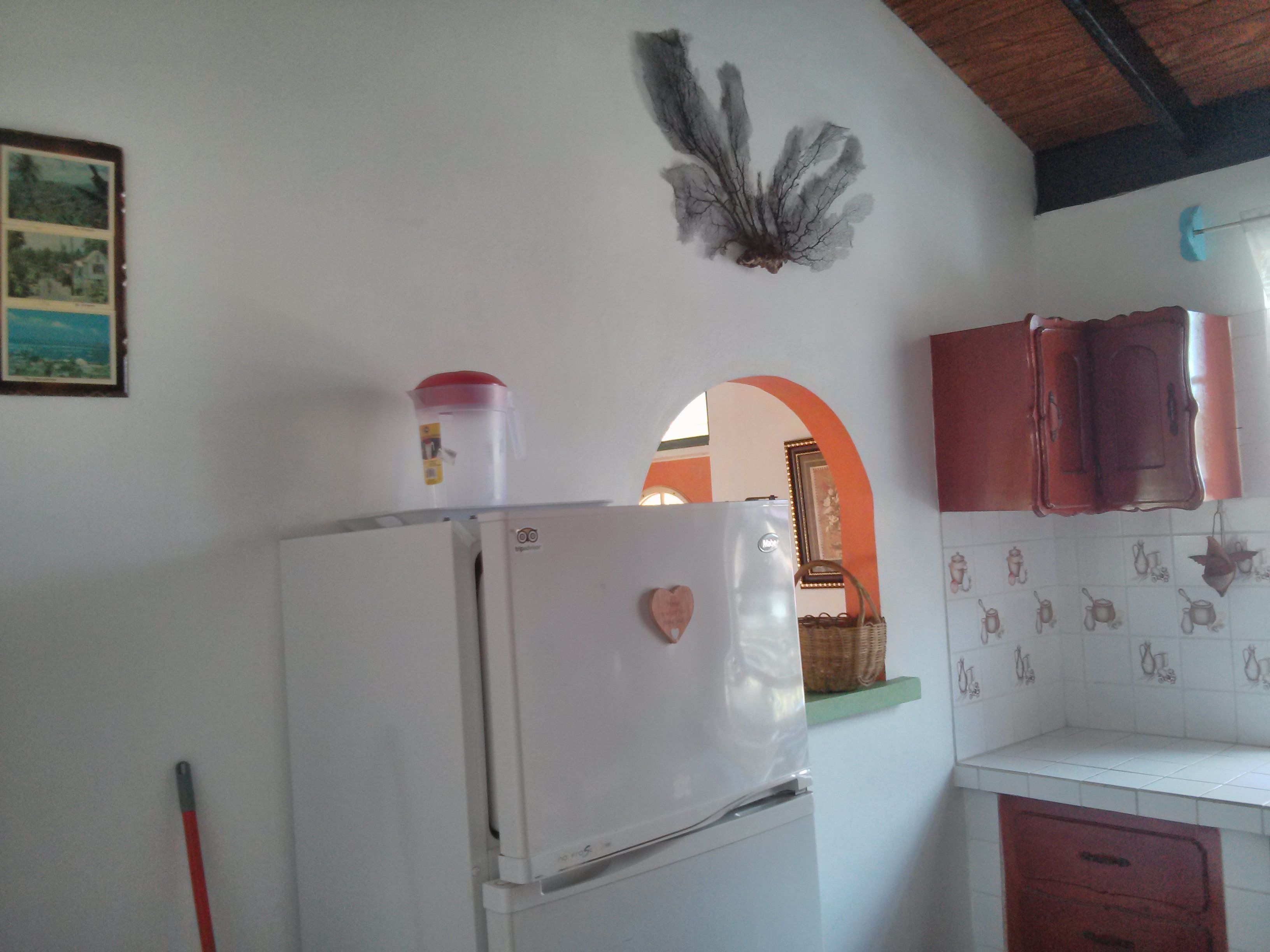 Cozinha com geladeira branca, um recipiente vermelho em cima e um enfeite em formato de coração na geladeira.