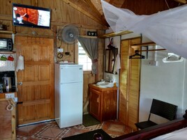 Una cocina compacta con armarios de madera, un refrigerador blanco, un lavamanos pequeño y un televisor montado en la pared.