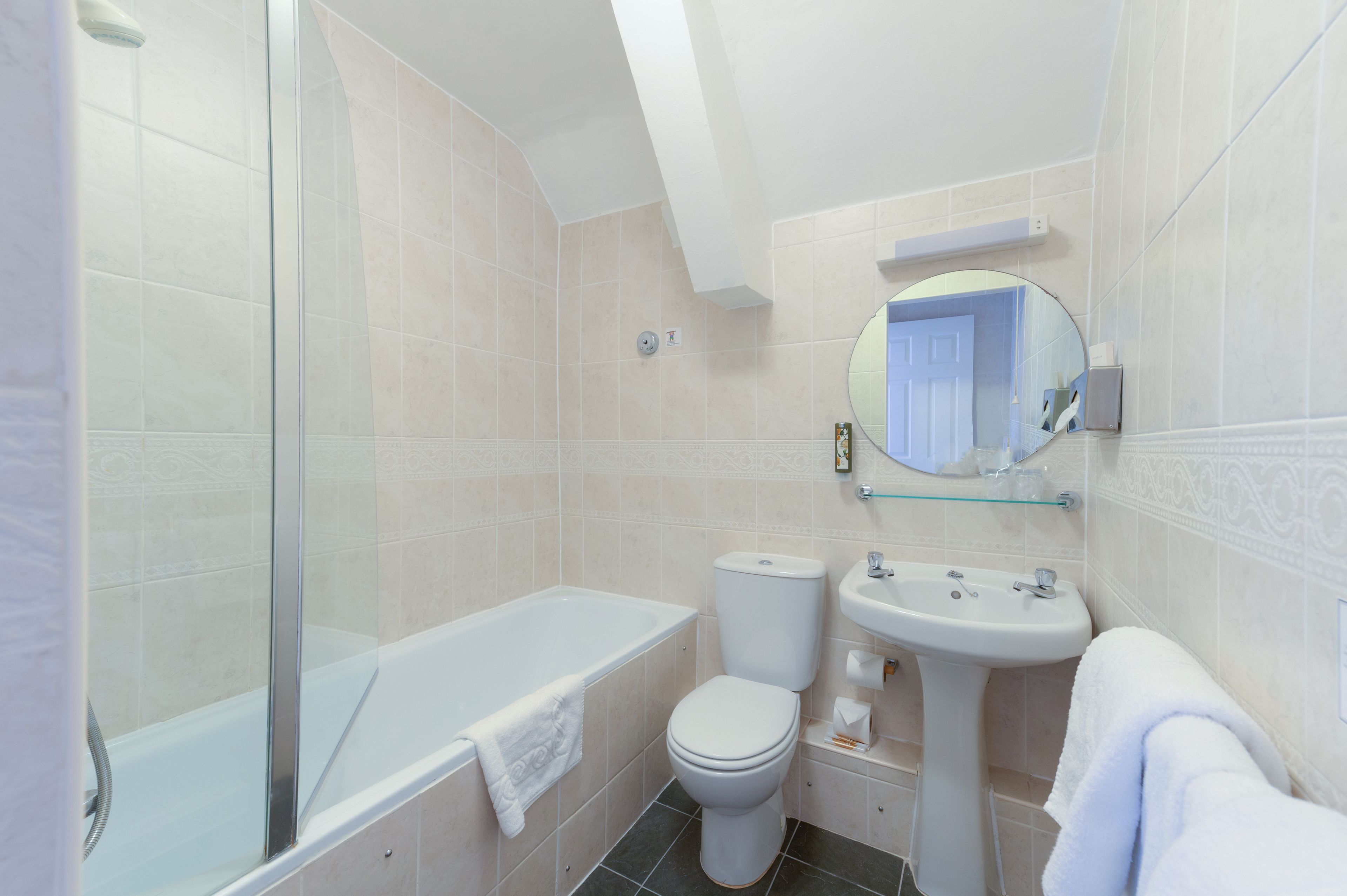 A modern bathroom with a glass-enclosed shower, a white bathtub, a toilet, and a sink with a mirror above it.