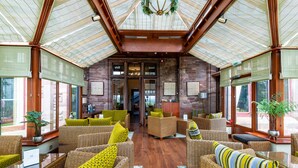 A spacious lobby with wicker furniture, large windows, and a high ceiling with a glass roof.