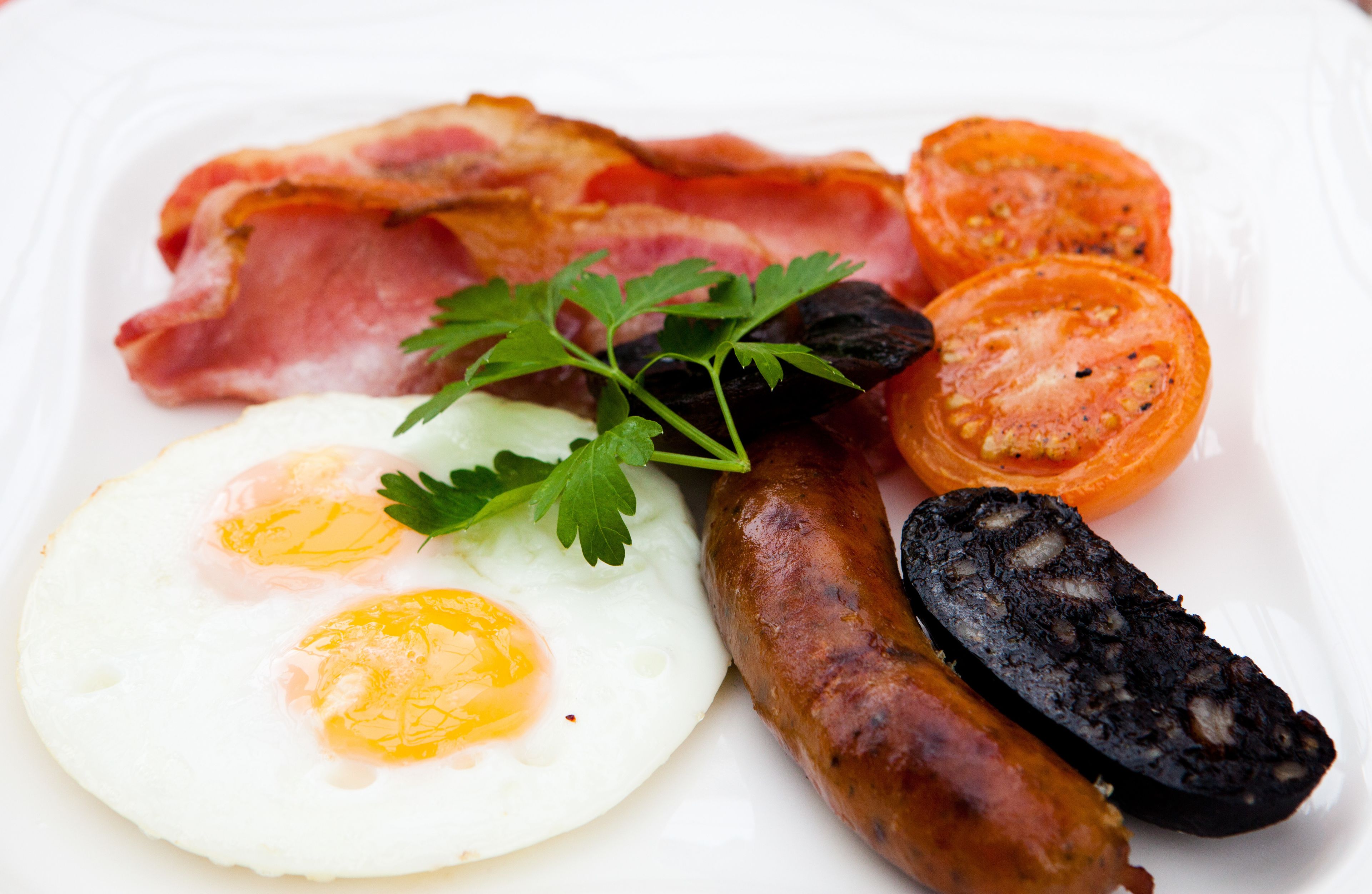Une assiette de petit-déjeuner avec des œufs, du bacon, des saucisses et des tranches de tomates.