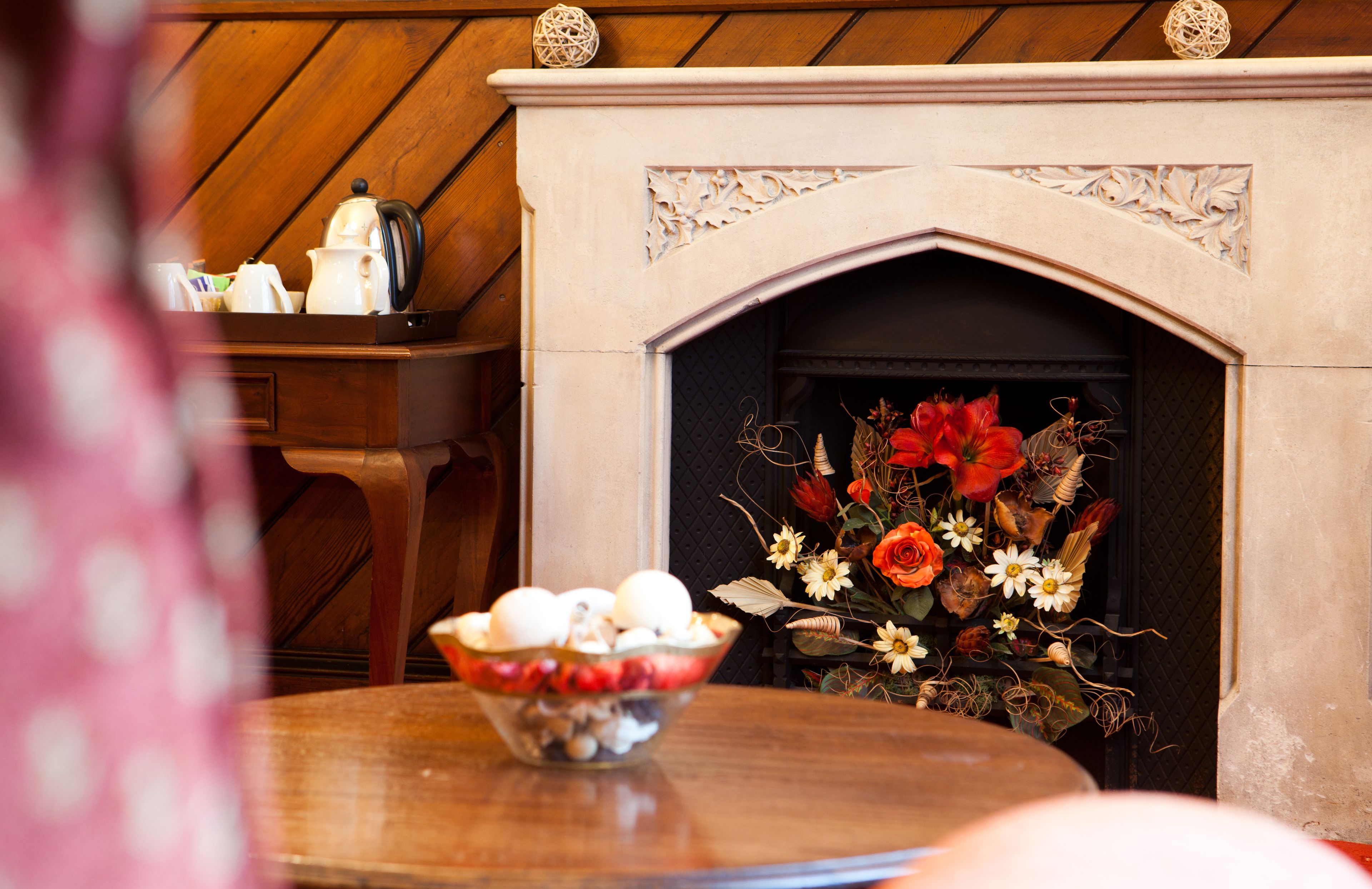 Una mesa de madera con un cuenco de fruta y una chimenea decorada con flores.