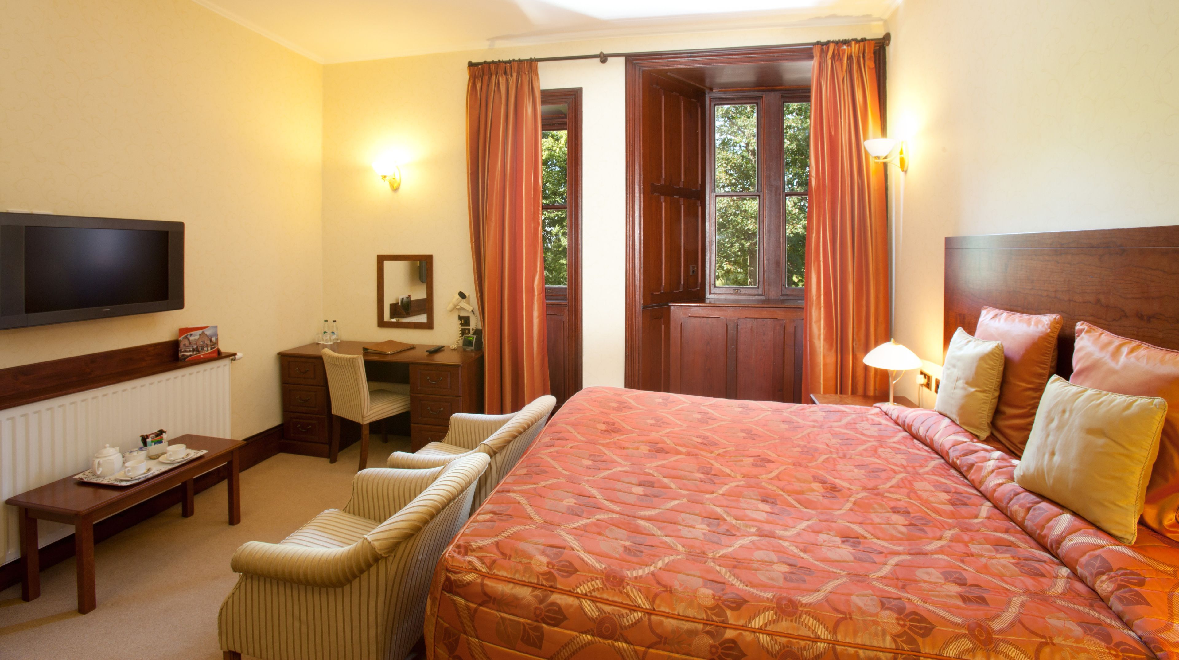 A hotel room with a large bed, a desk with a chair, a television mounted on the wall, and a window with curtains.