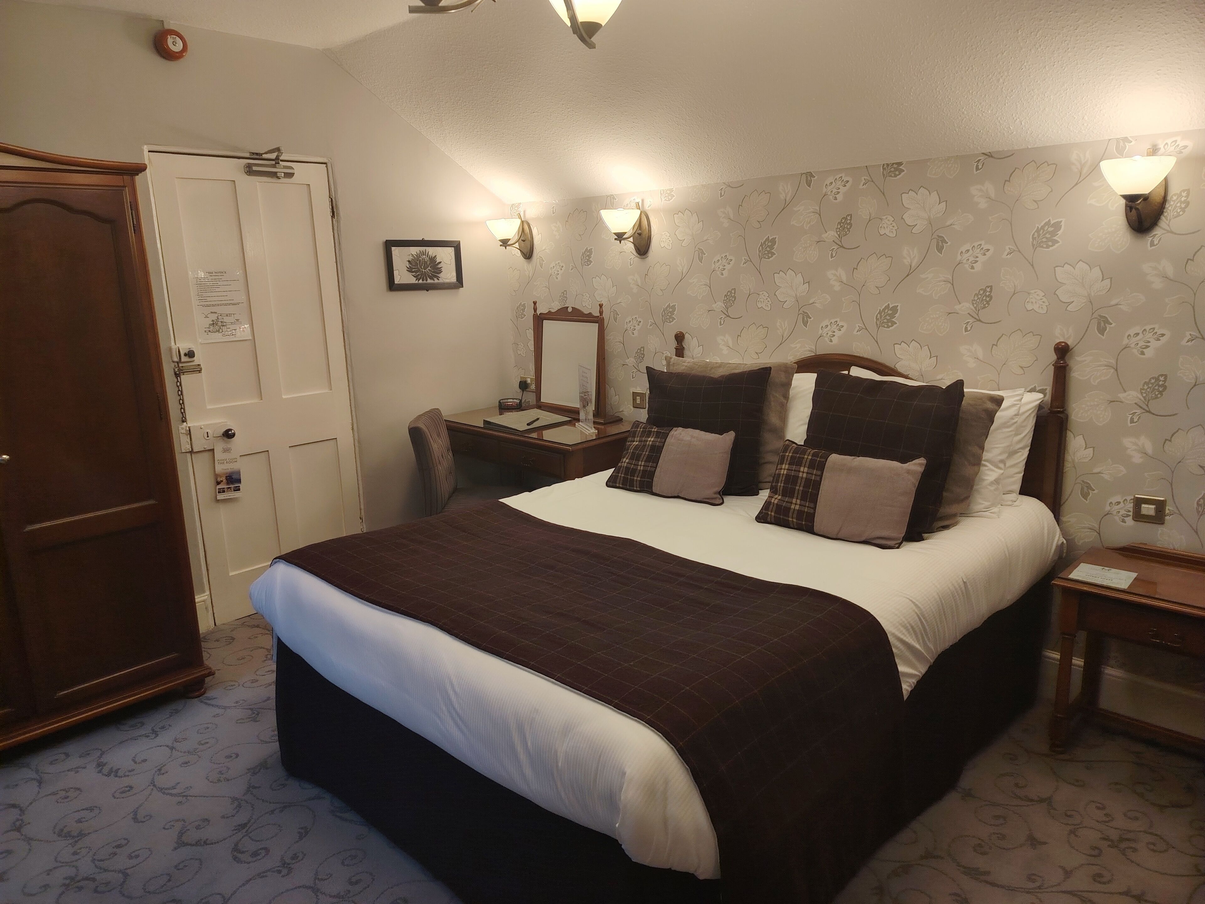 Habitación de hotel con una cama grande, un escritorio, una silla, un armario y una lámpara fijada a la pared.