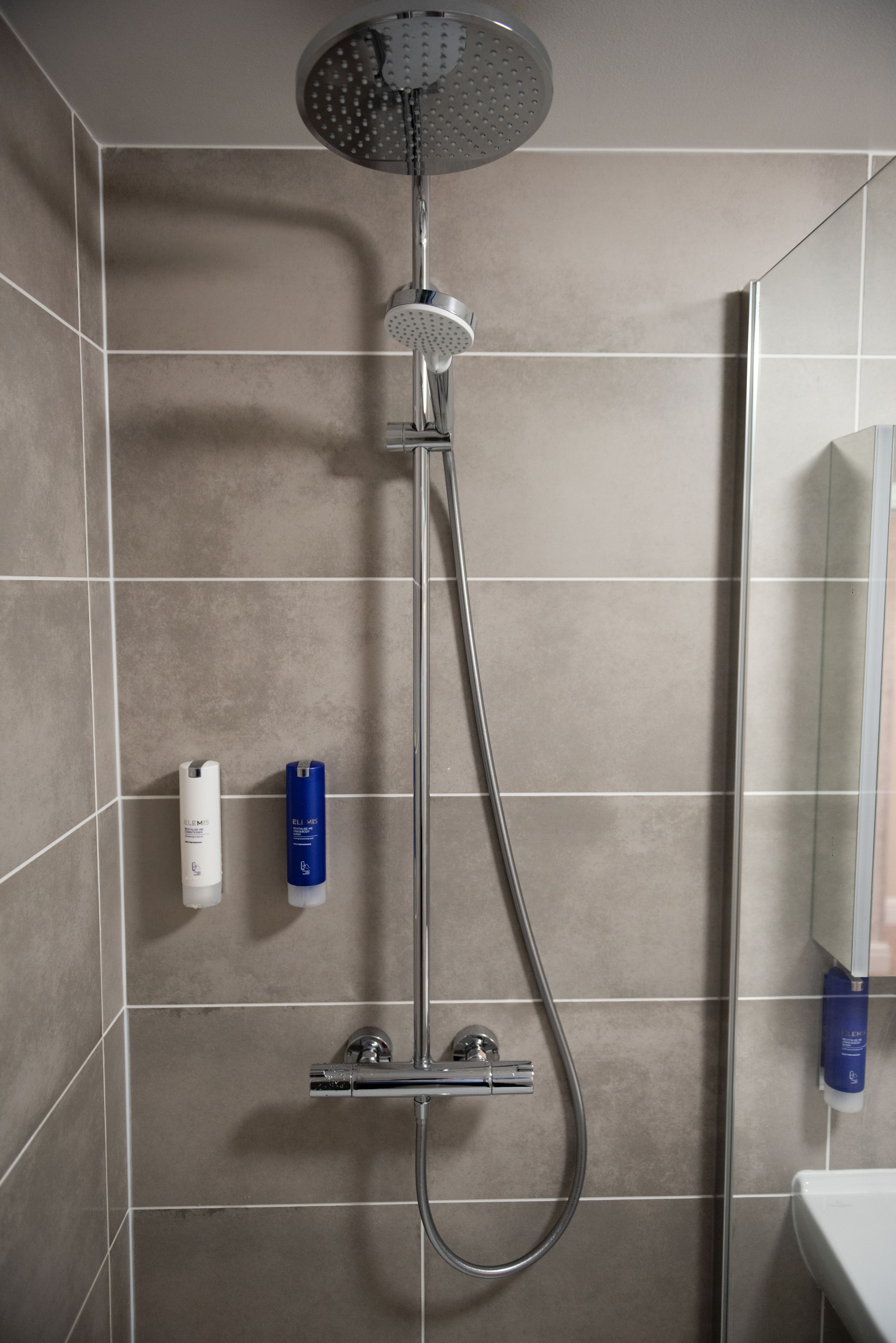 A shower with a handheld showerhead and a wall-mounted control panel.