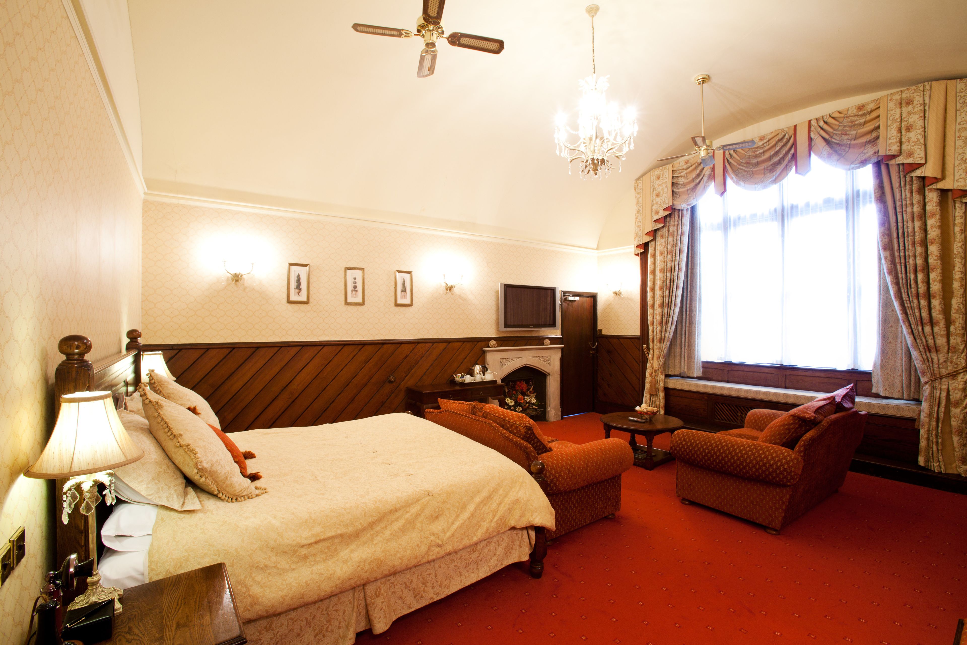 Habitación de hotel con cama, sofá, televisión, chimenea y candelabro.