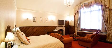 Habitación de hotel con cama, sofá, televisión, chimenea y candelabro.