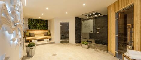 A modern lobby with a wooden bench, a reception desk, and a glass door leading to a sauna area.