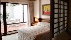 A bedroom with a bed, a nightstand, a painting on the wall, and a sliding glass door leading to an outdoor area with a table and chairs. - Suites Real 85 (Bogota)