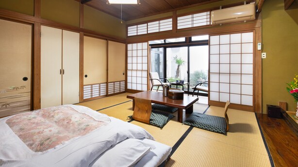 A traditional Japanese room with tatami flooring, a bed with floral bedding, a wooden table, and sliding doors. - Daibutsu Ryokan (Takaoka)