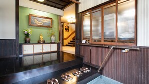 A reception area with a wooden staircase, a green wall with artwork, and a wooden railing. - Daibutsu Ryokan (Takaoka)
