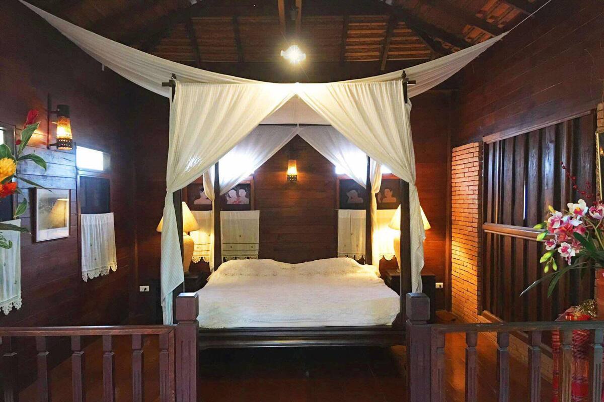 A wooden room with a bed under a canopy, wooden walls, and a small table with a lamp.