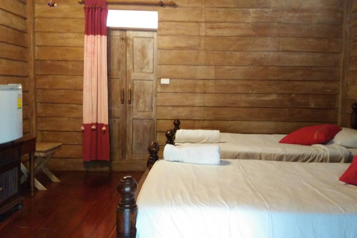 A wooden room with two beds, a wooden wardrobe, a small table, and a red curtain.