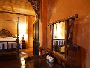 A hotel room with a four-poster bed, a nightstand with a lamp, a mirror, and a small table with decorative items. - Baan Singkham Resort (Chiang Mai)