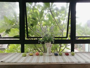 A window with a view of green foliage, a white vase with flowers, and a row of small toy cars on a striped mat. - Baan Singkham Resort (Chiang Mai)