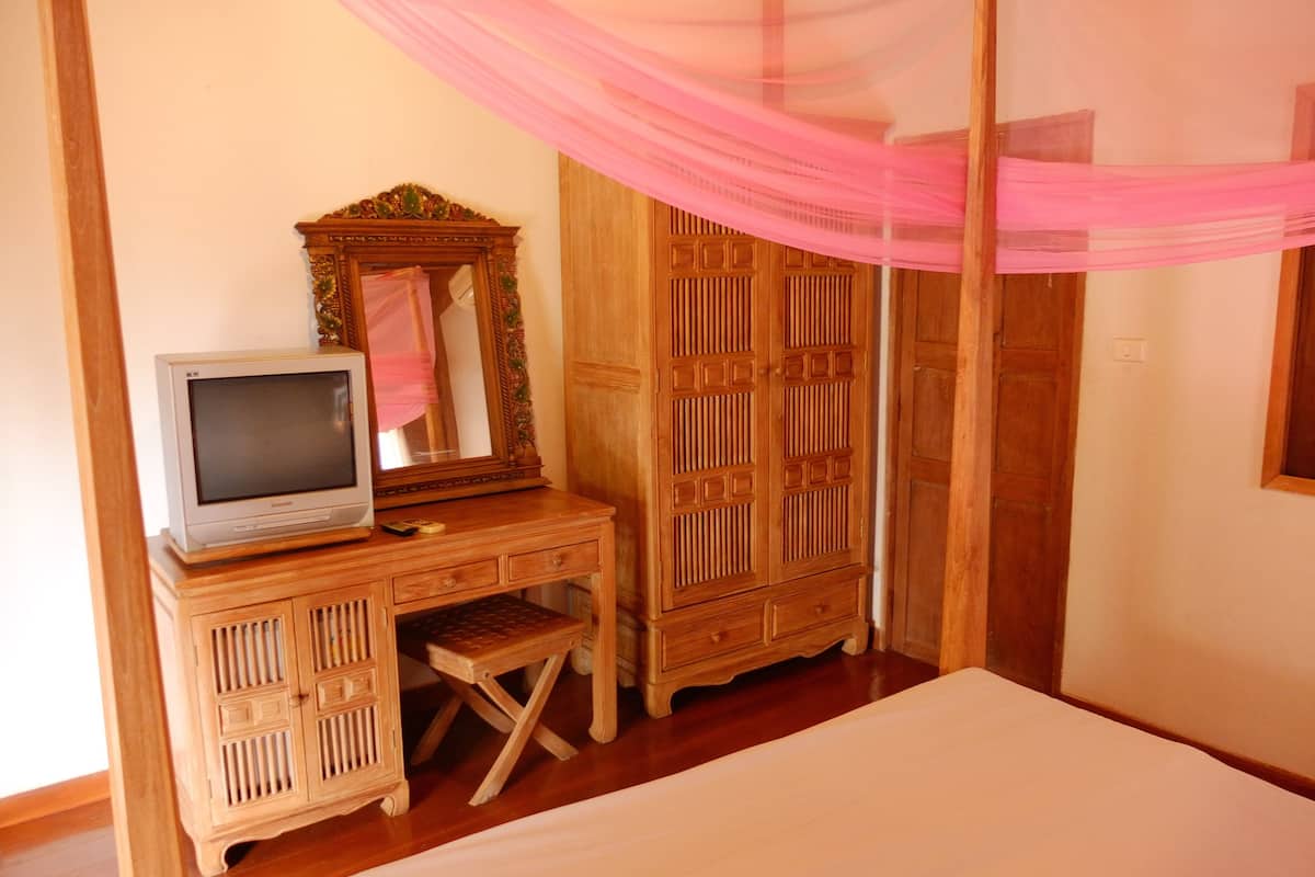 A bedroom with a bed, a wooden dresser, a television, and a mirror.