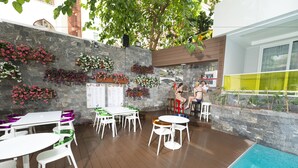A poolside area with white tables and chairs, a stone wall with flower boxes, and a view of the pool. - Kleopatra Suit Hotel  (Alanya)