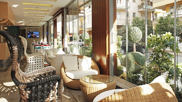 A spacious indoor area with wicker furniture, large windows, and a view of the street. - Kleopatra Suit Hotel  (Alanya)