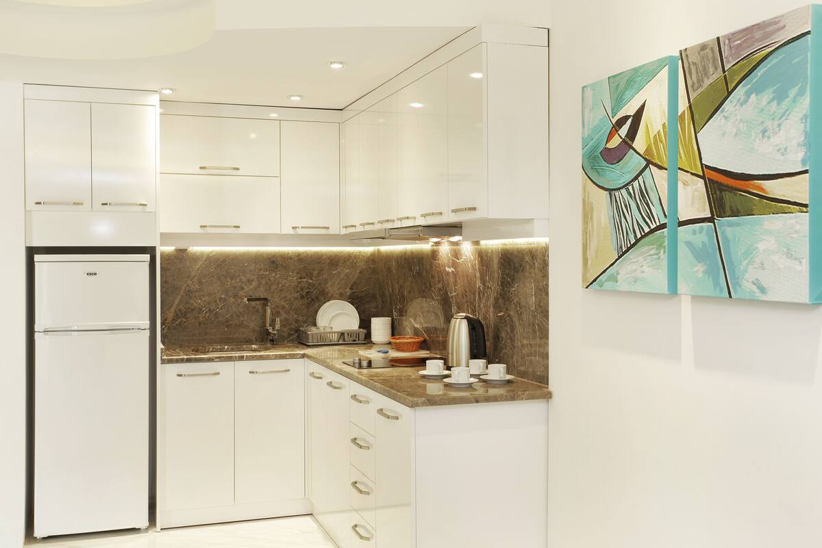 A modern kitchen with white cabinetry, a marble countertop, and a coffee maker.