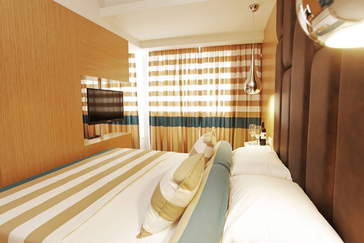 A hotel room with a bed, a television on the wall, and curtains.