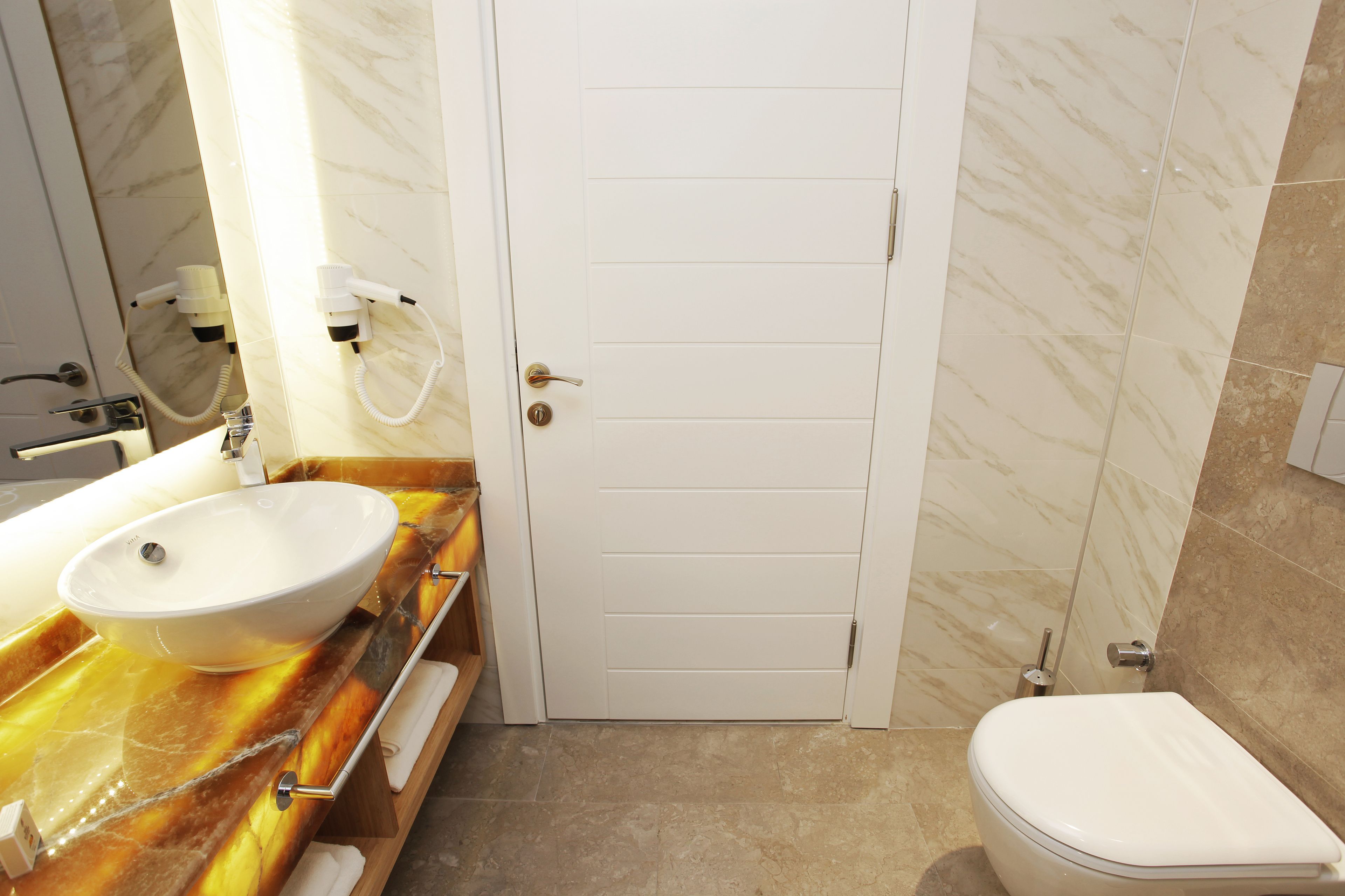 Une salle de bain avec un lavabo blanc, des toilettes et une porte dotée d’une poignée.