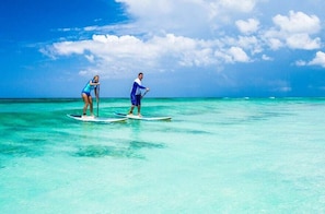 Two people paddleboarding on a clear turquoise sea with a bright blue sky.