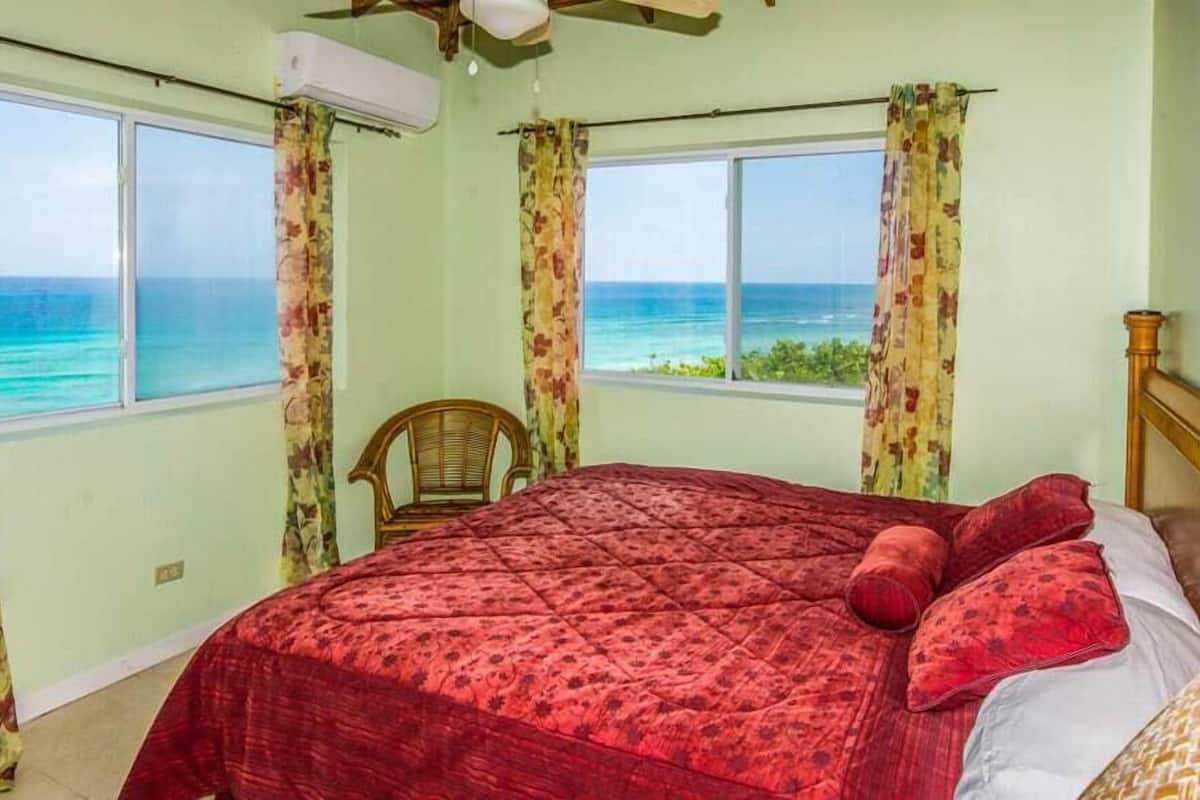 A room with a bed, a chair, and a view of the ocean.
