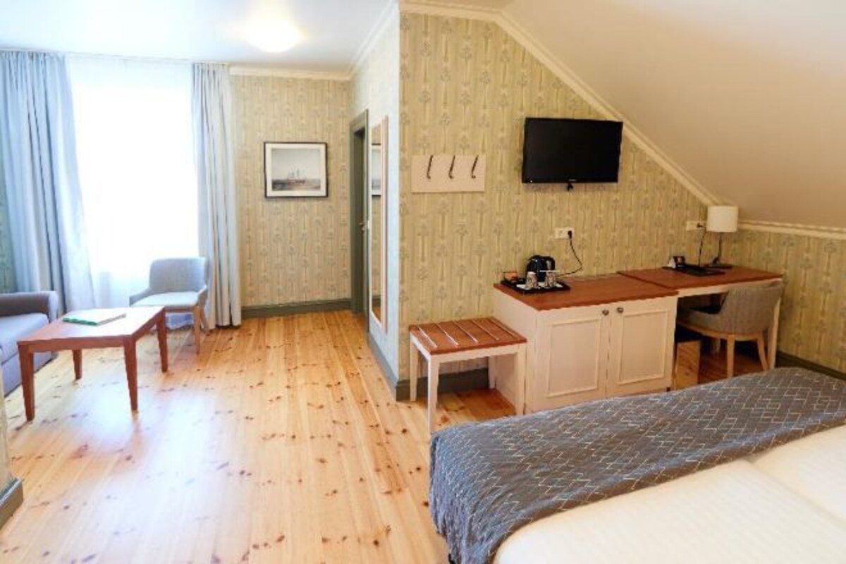A hotel room with a bed, a desk, a chair, a small table, a television, and a window with curtains.