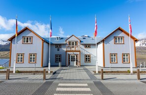 A two-story building with a central entrance, flanked by two wings, each with a flagpole. - Fosshotel Eastfjords (Fjardabyggd)