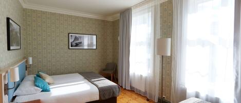 Une chambre d’hôtel avec deux lits, une chaise, une table de chevet avec une lampe et une fenêtre avec des rideaux.