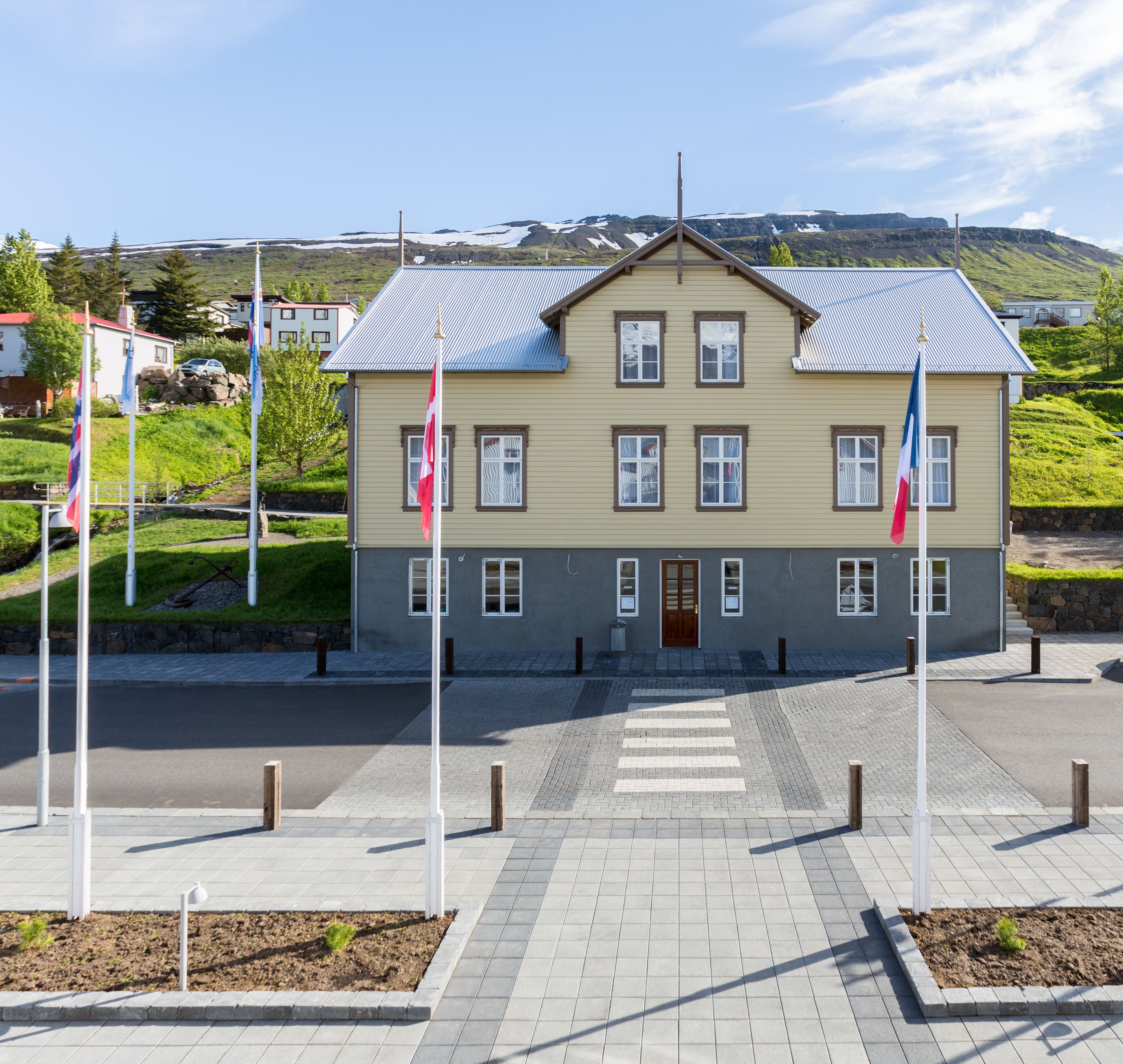 A two-story building with a symmetrical facade, a central entrance, and a paved area in front.