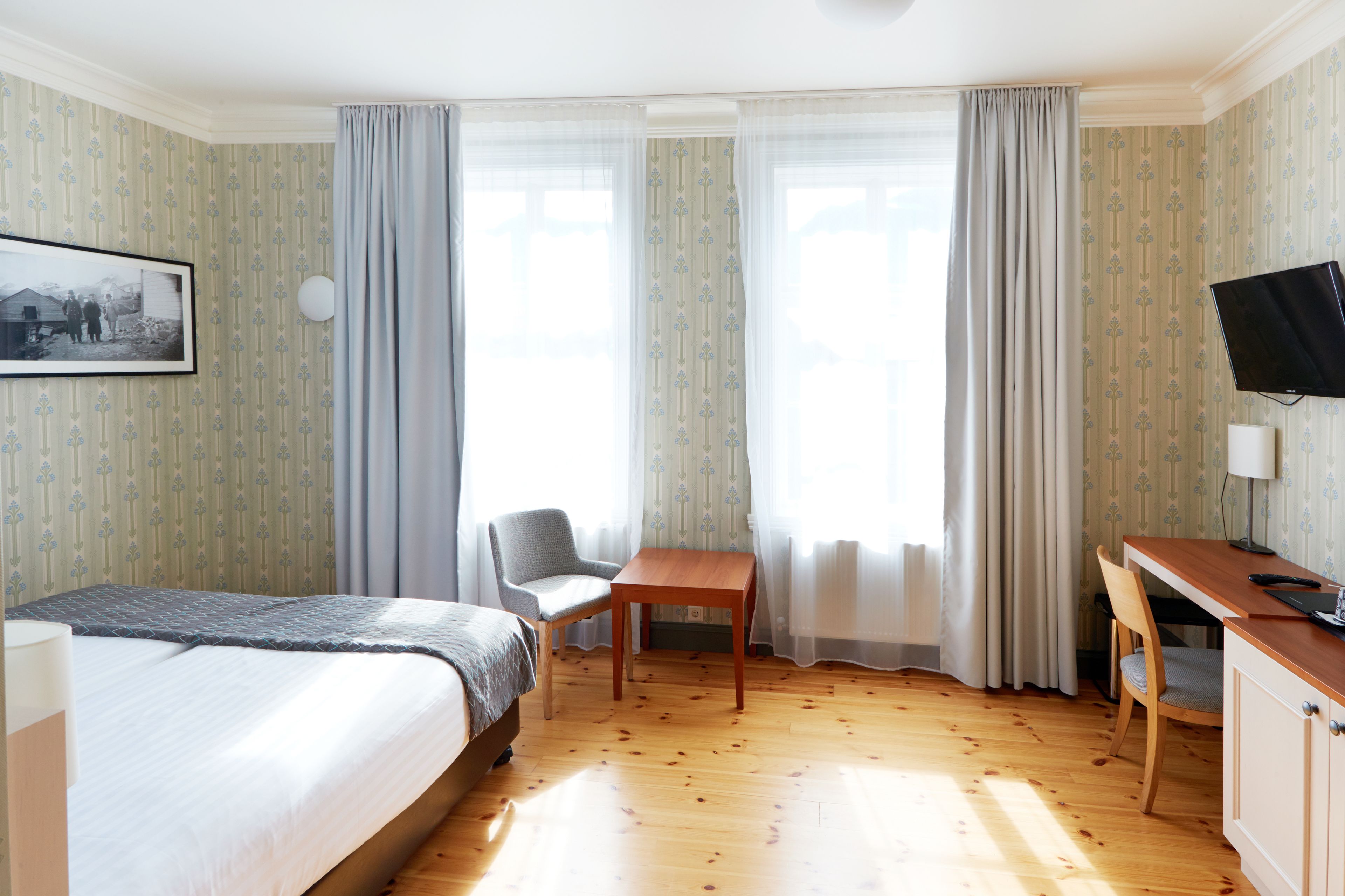 A hotel room with a bed, a desk, a chair, and a television.