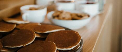A breakfast buffet with pancakes, bowls of food, and a coffee machine.